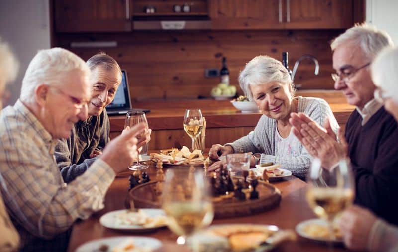 5 seniors sitting around table enjoying dinner