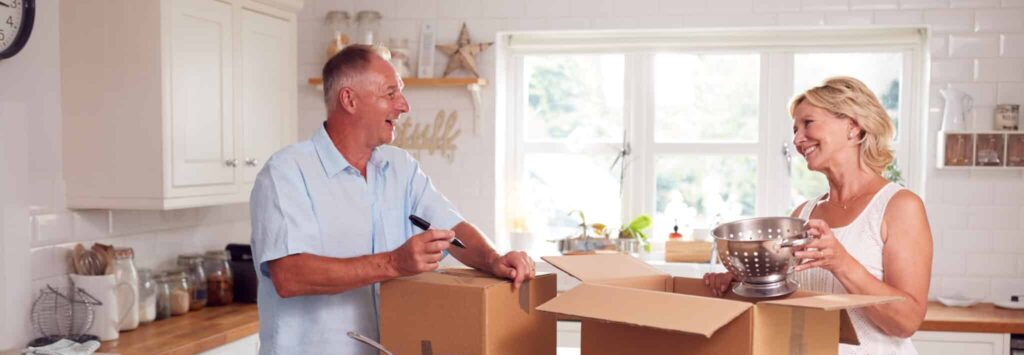 Senior Couple Downsizing In Retirement Packing And Labelling Boxes Ready For Move Into New Home